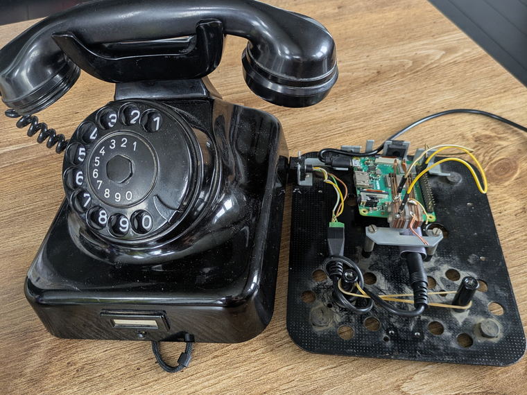The reassembled black rotary telephone standing beside its base plate, which has a Raspberry Pi and wiring mounted on it.