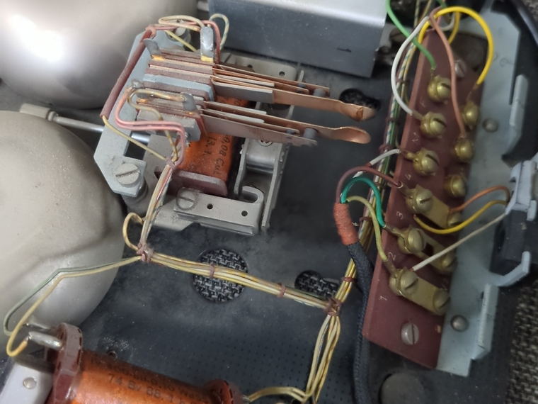 The inside of the phone base: a stack of copper leaf contacts, a terminal block with brass screws and coloured wires, an induction coil and a foil capacitor.