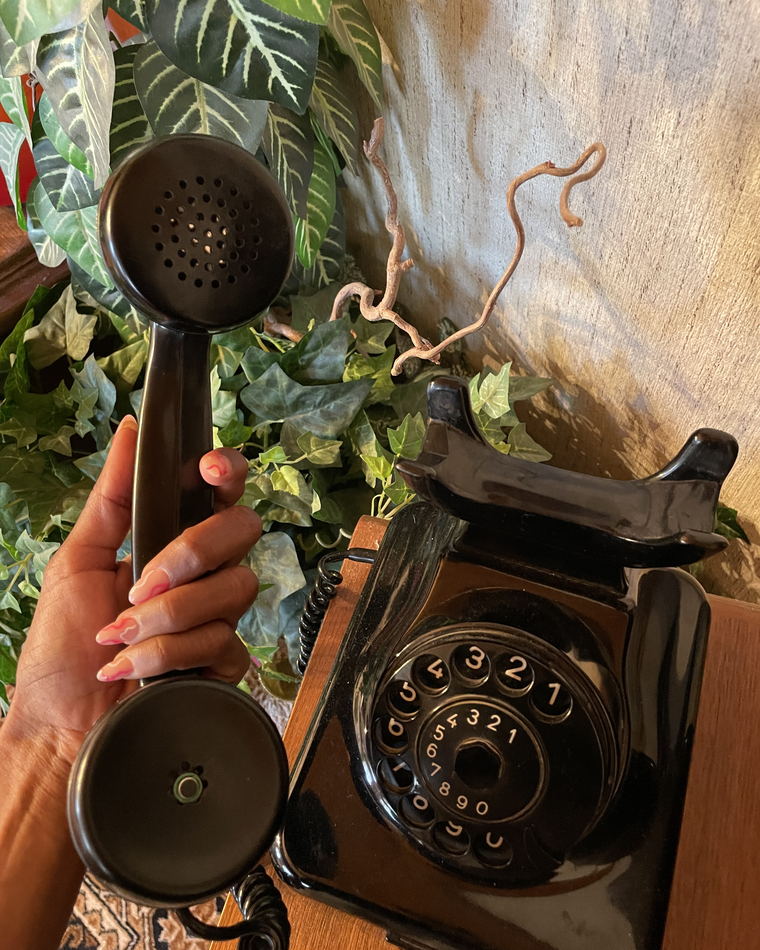 A hand holding the telephone handset up by its earpiece, with the dial of the phone visible below.